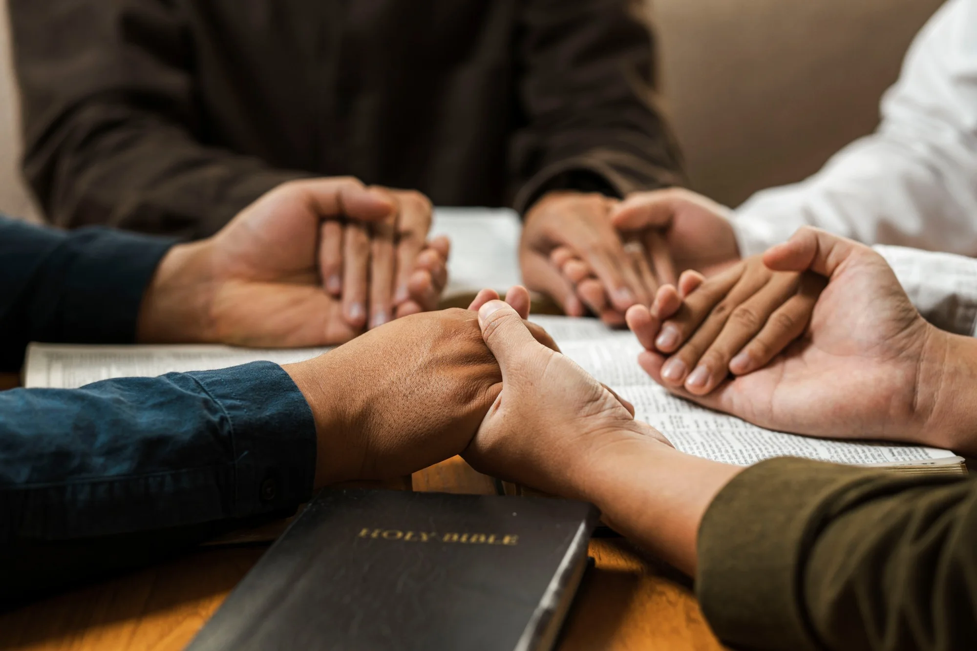 Four people around a table with open Bibles, hands joined in prayer