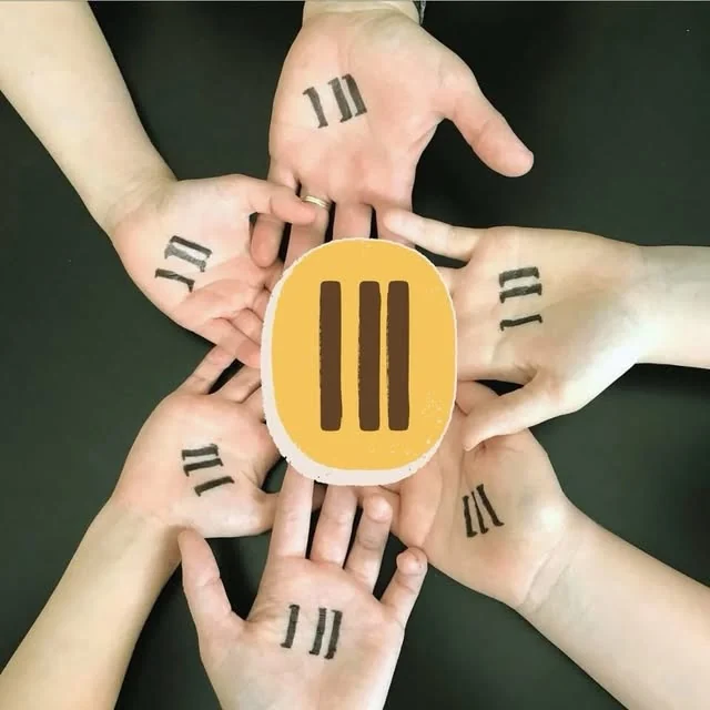 Hands arranged in a circle, each marked with the A Third of Us three-line symbol, around the movement’s badge