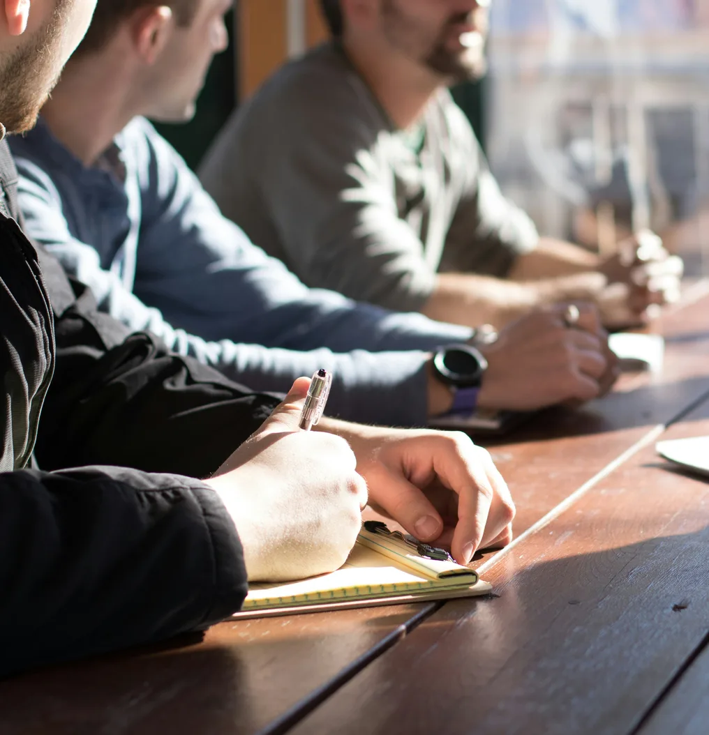 Colleagues taking notes around a table in a sunlit meeting